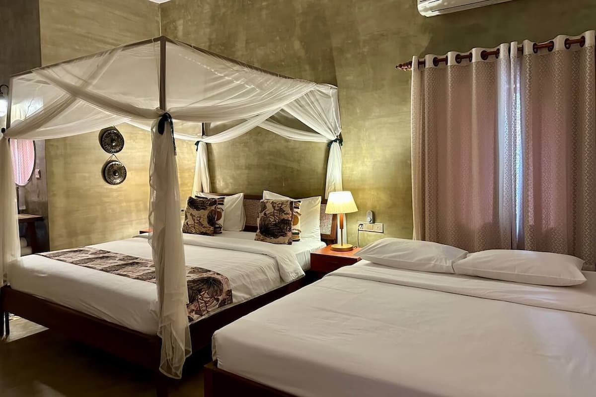 A room with a four-poster bed, a bedside table with a lamp, and a wall-mounted air conditioner.