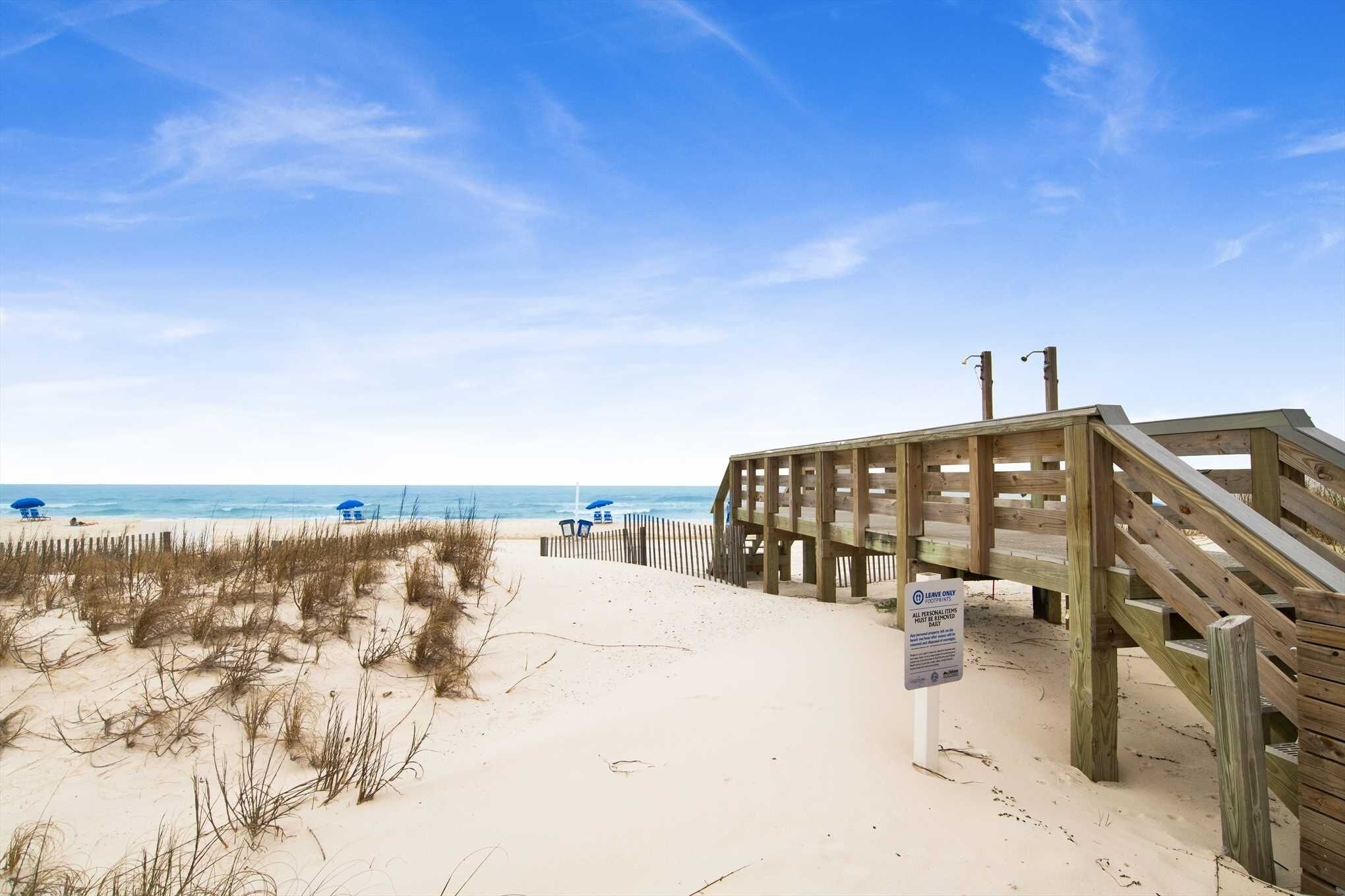 A beach with a wooden boardwalk, a sign, and beach umbrellas.