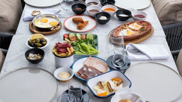 A breakfast table set with various dishes, including eggs, meats, and vegetables, in a room with a large window and cushioned seating. - Stayso The House Hotel (Istanbul)
