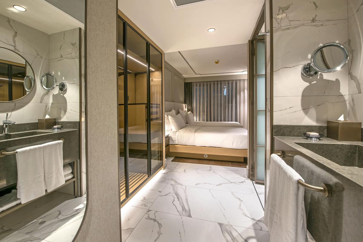 A modern hotel room with a marble bathroom, a large bed, and a glass partition.