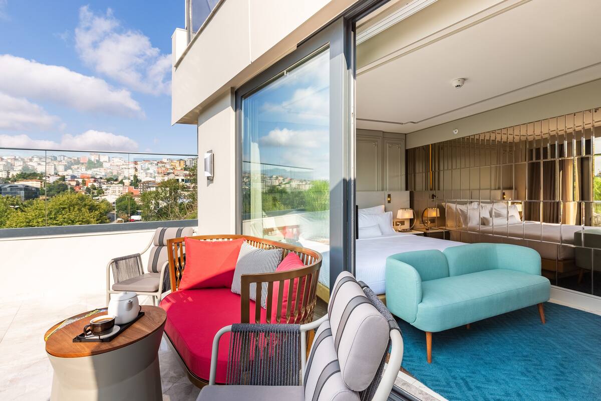 A modern hotel room with a balcony, a bed, a sofa, and a seating area with a coffee table.