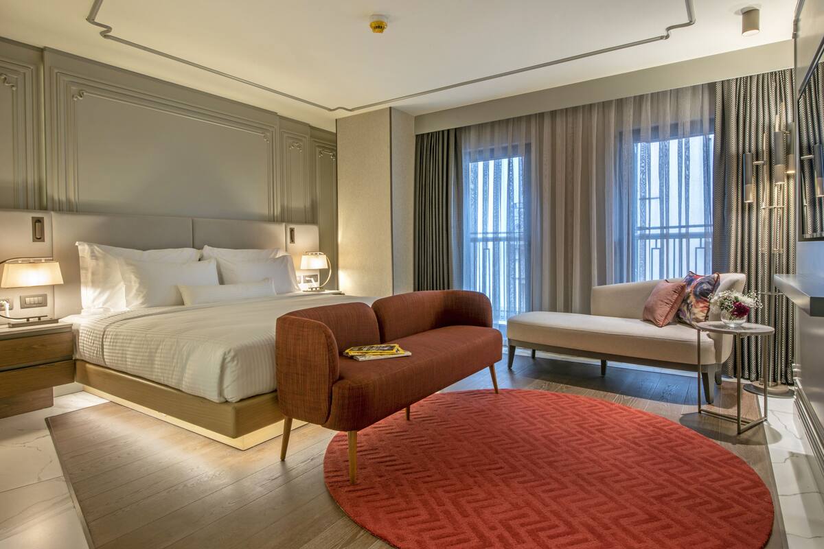 A hotel room with a large bed, a sofa, a red rug, and a small table with a vase.