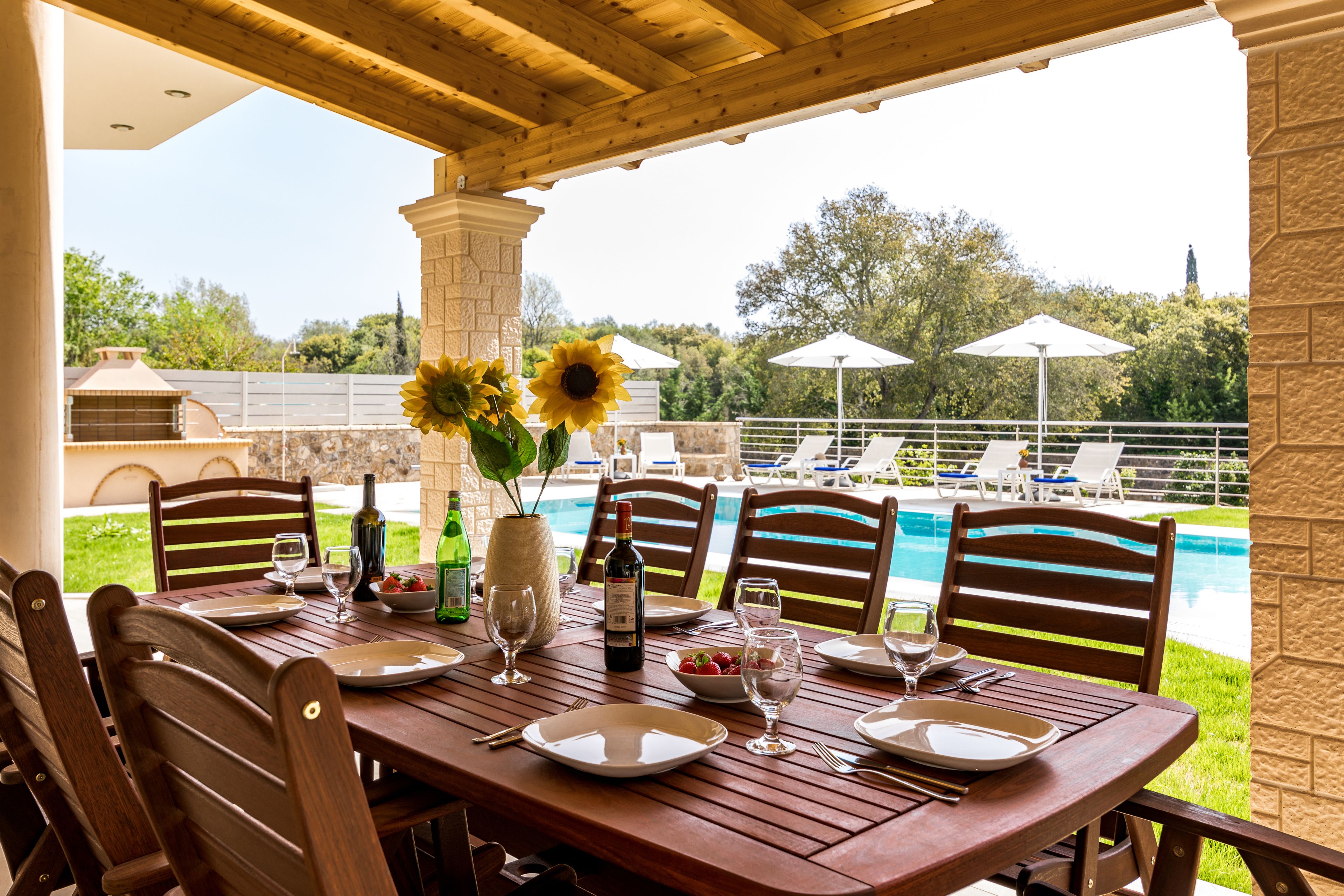 A wooden dining table set for six with a view of a pool and lounge chairs.