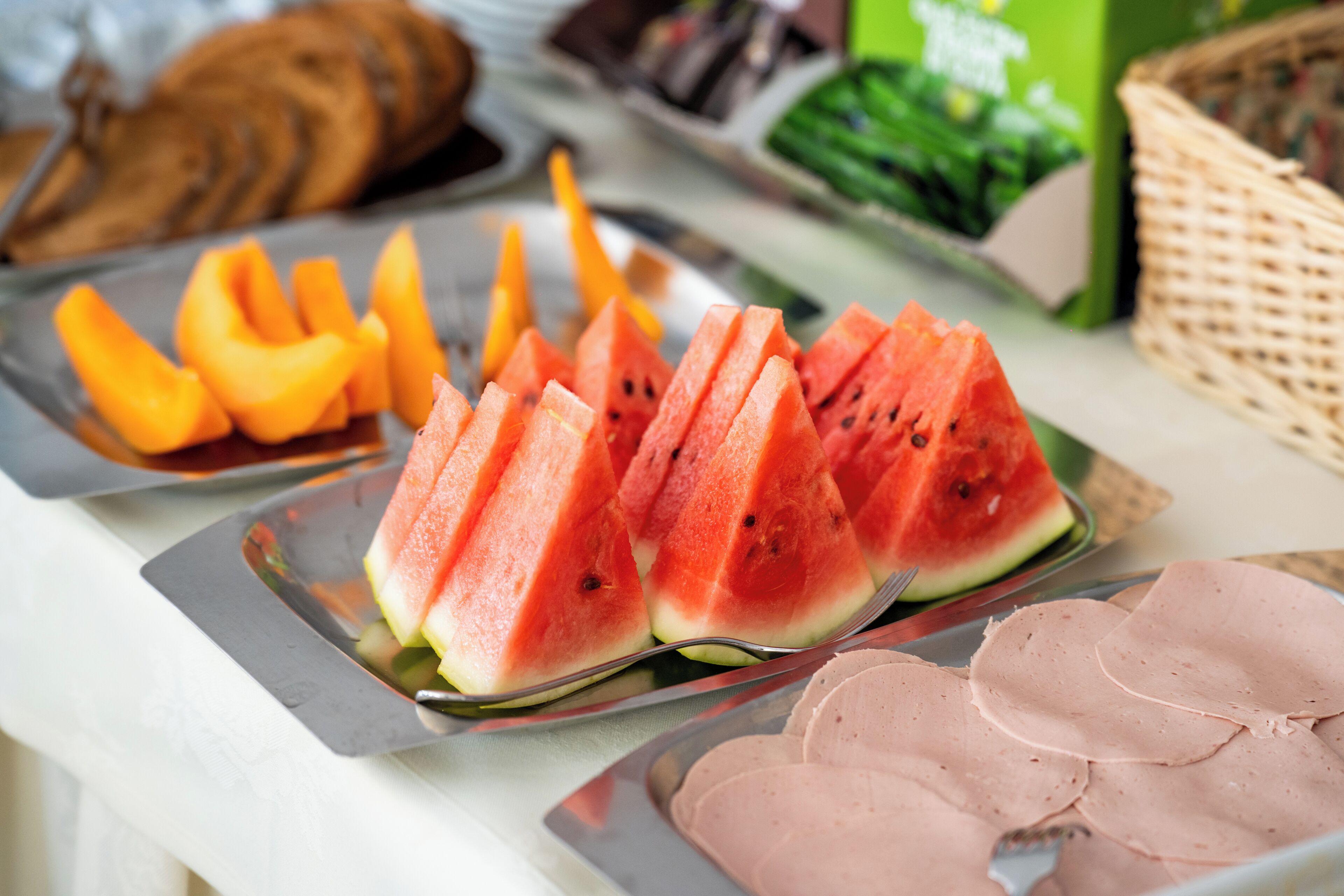 A buffet with watermelon slices, ham, and other food items.