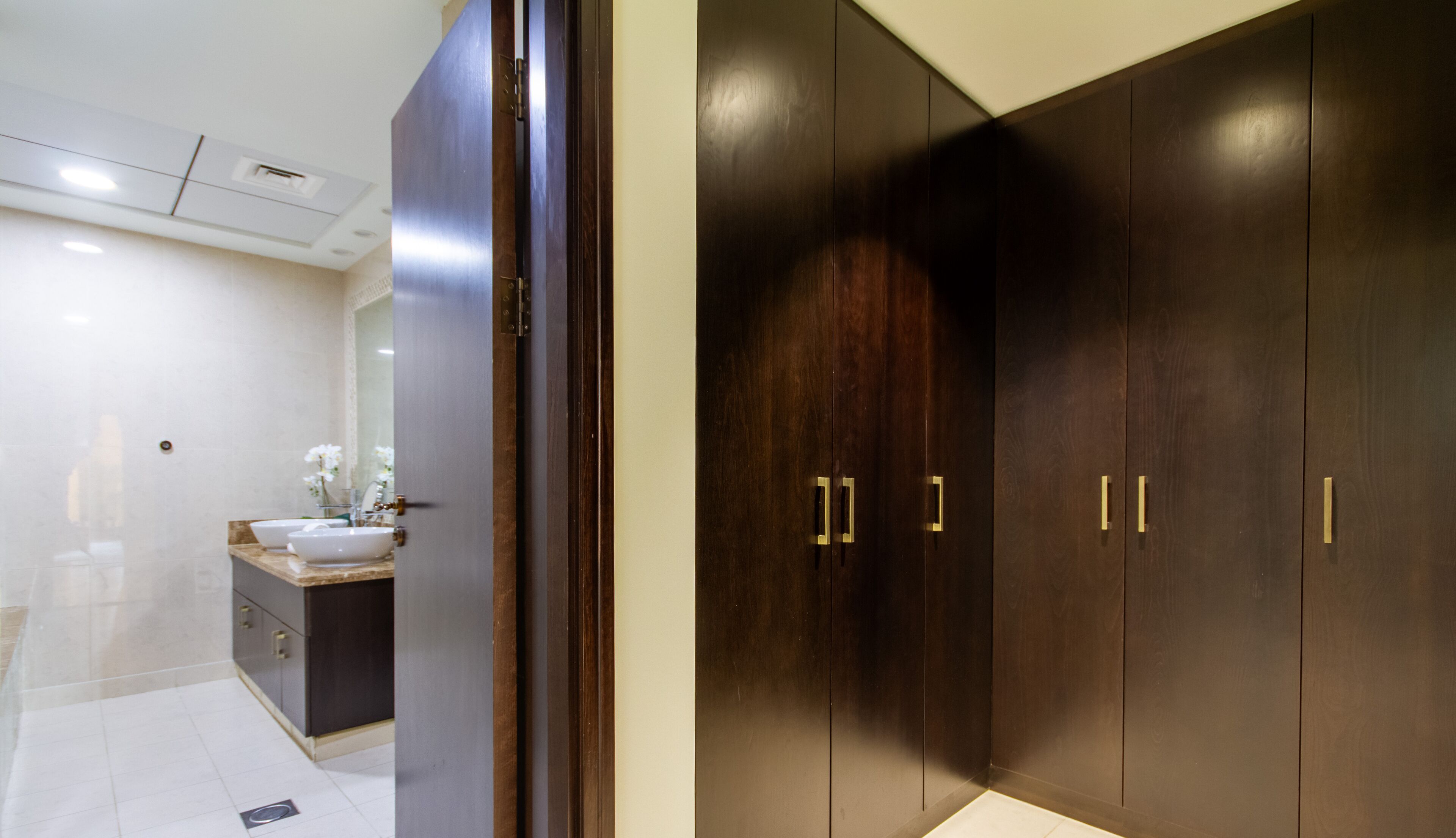A modern bathroom with a large mirror, a sink, and a dark wooden wardrobe with gold handles.