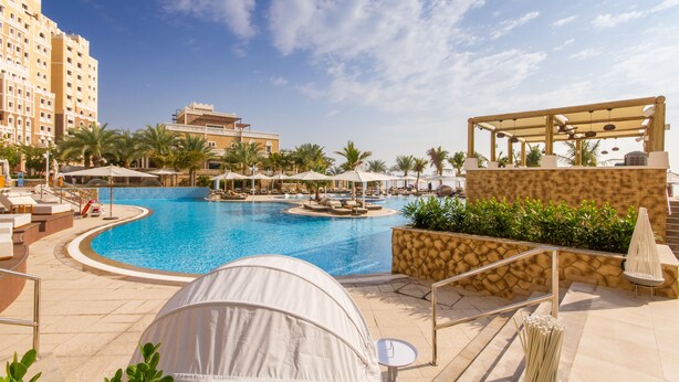 Zwembadgedeelte van een resort met ligbedden, parasols en een tent.