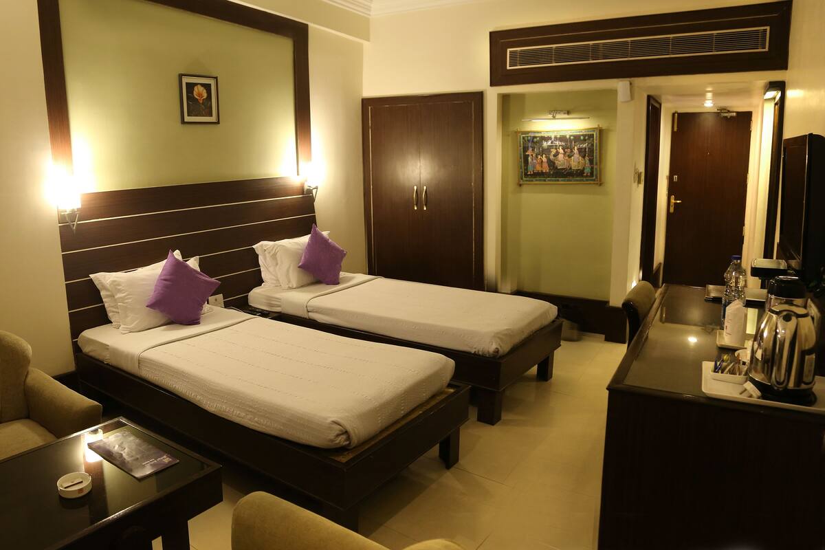 A hotel room with two single beds, a small table, a chair, a desk, and a minibar.