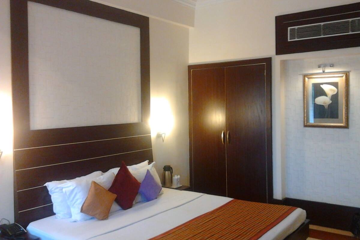 A hotel room with a large bed, a wardrobe, a framed picture on the wall, and a bedside table with a lamp.