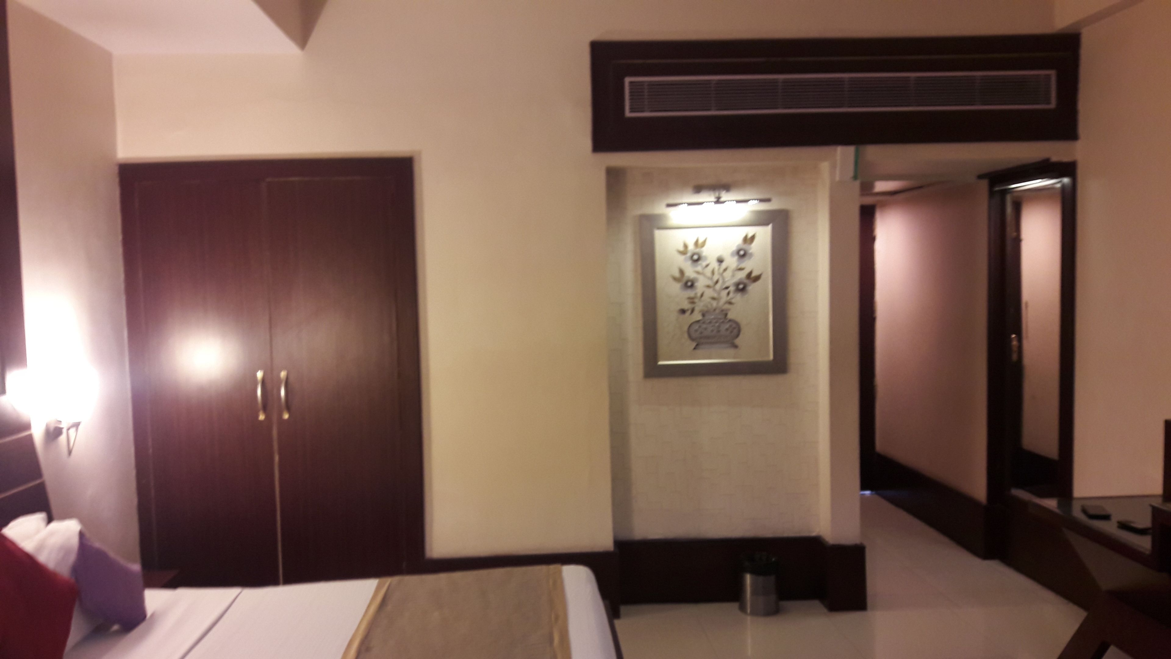 Quarto de hotel com um guarda-roupa espaçoso, uma obra de arte emoldurada acima da porta e um pequeno cesto de lixo no chão.