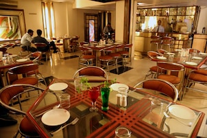 Un restaurante con varias mesas y sillas, una zona de bar con botellas, y algunos clientes sentados.