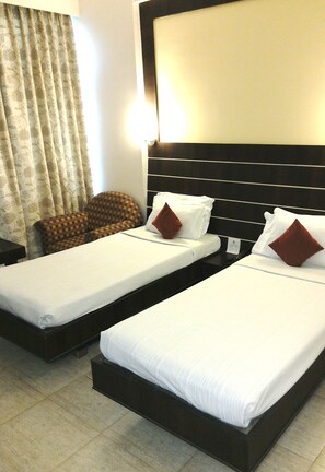 Two single beds with white linens and brown pillows, a checkered armchair, and a large wall-mounted TV. - Hotel Satya Ashoka (Jabalpur)