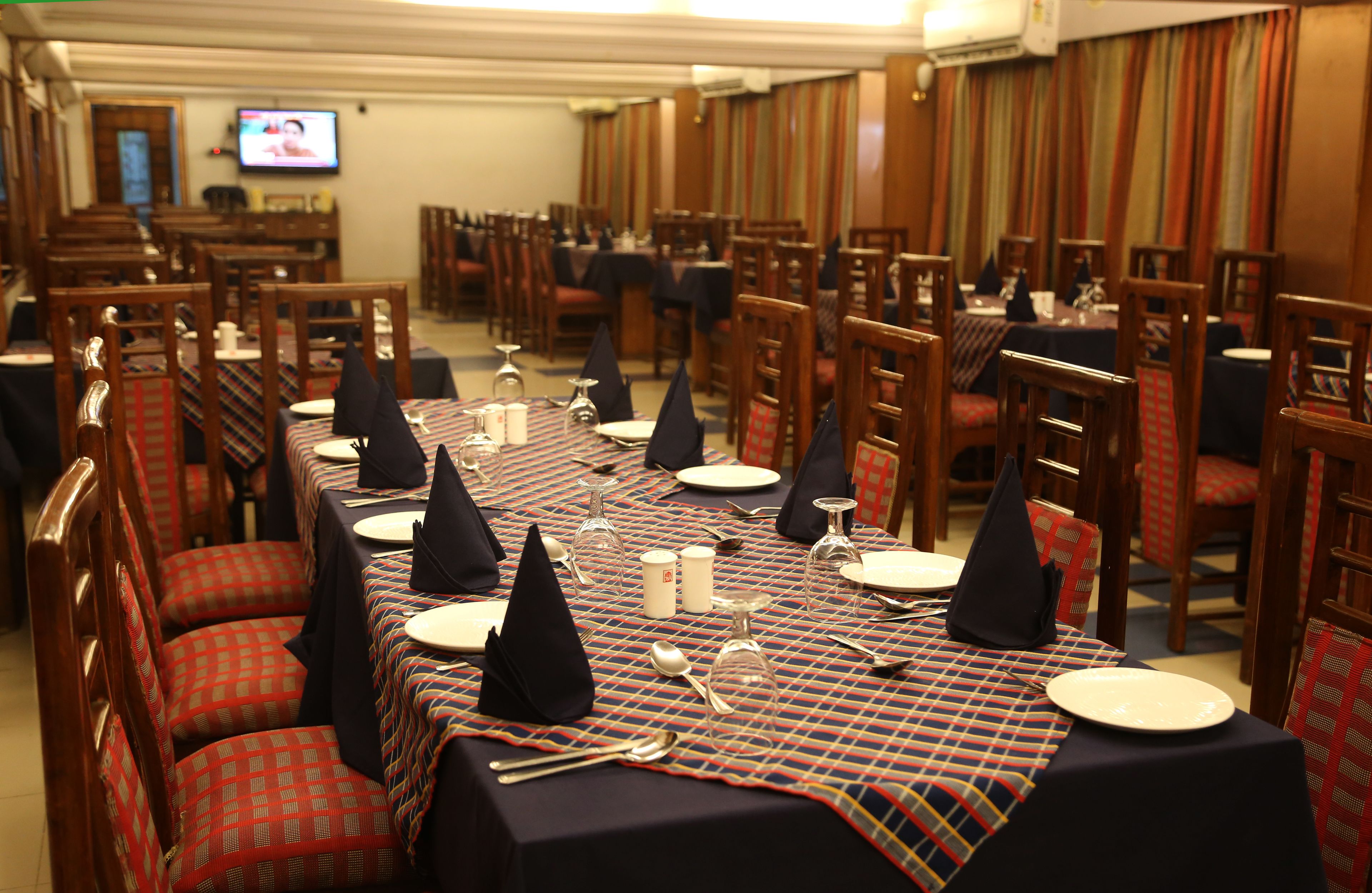 A dining area with multiple tables set for service, each with a tablecloth, napkins, and cutlery.