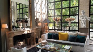 A cozy living room with a fireplace, a sofa with colorful cushions, a coffee table with books, and large windows with a view of greenery. - Le Complot - Maison Privée à Avignon (Avignon)