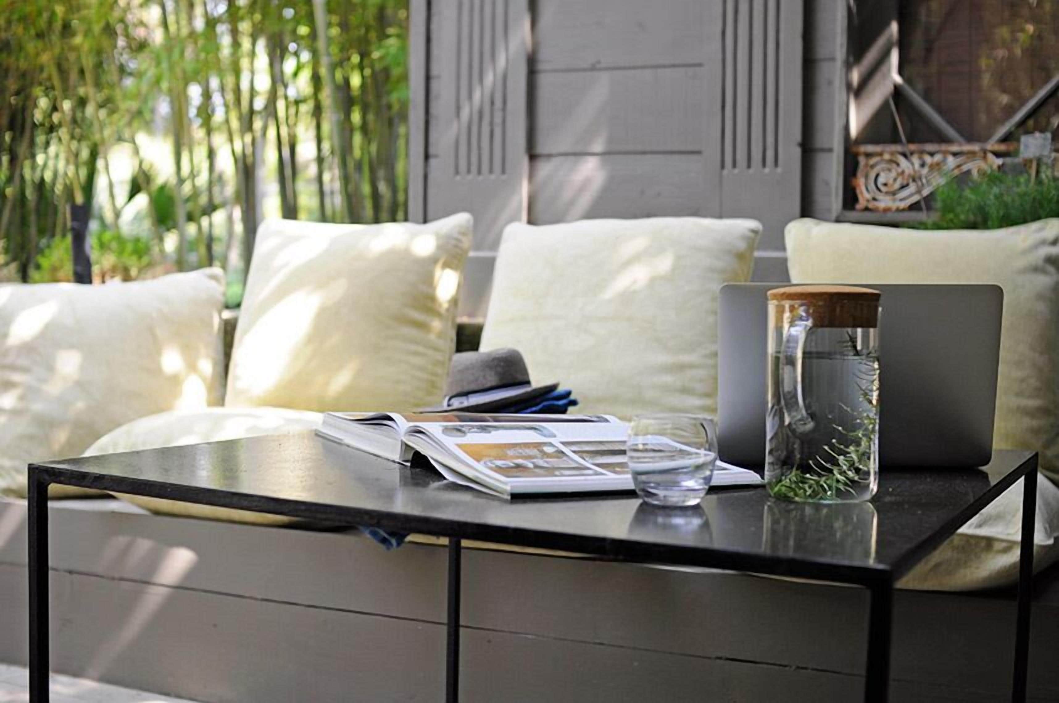 Un espacio al aire libre moderno con una mesa de vidrio, libros, una computadora portátil y un tarro de vidrio con hierbas.