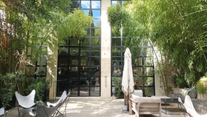 An outdoor seating area with modern chairs and a table, surrounded by lush greenery and a large glass door entrance. - Le Complot - Maison Privée à Avignon (Avignon)