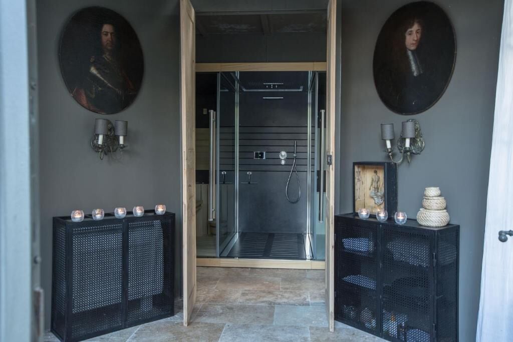 A modern bathroom with a glass shower enclosure, two wall-mounted sconces, and a decorative cabinet with candles.