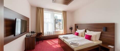 Habitación de hotel con una cama grande, un escritorio, un televisor y una ventana con cortinas.
