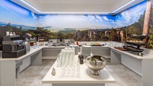 Cocina moderna con un mural panorámico, preparación tipo buffet y máquinas de café.