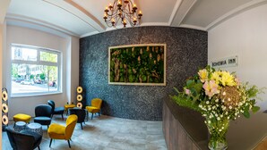 Un área de recepción con diseño moderno, que presenta una araña, una obra de arte grande colgada en la pared y un jarrón con flores.
