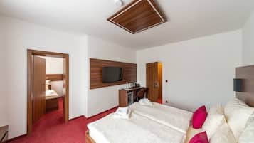Habitació d'hotel amb llit, escriptori, televisió penjada a la paret i un passadís amb moqueta vermella.