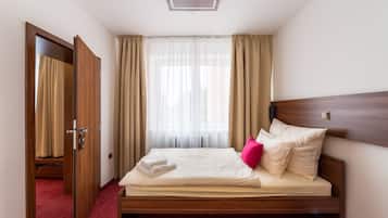 Un lit bien fait, avec du linge de lit blanc, une tête de lit en bois et un sol recouvert d’une moquette rouge.