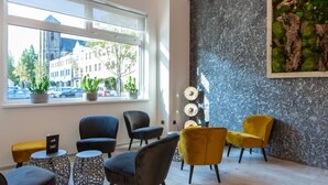 Un interior moderno con una zona de estar que incluye sillas negras y amarillas, una pared decorativa y vista a la calle a través de un ventanal grande.