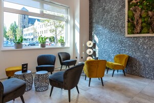 Um interior moderno com área de estar, destacando cadeiras pretas e amarelas, um painel decorativo e vista da rua através de uma grande janela.