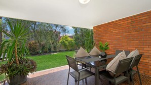 Une terrasse avec une table et des chaises, un mur en briques et une vue sur un jardin.