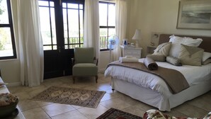 Un dormitorio con una cama, una silla, una mesita de noche, una lámpara y una ventana con cortinas.