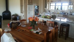 Un comedor amplio con una mesa y sillas de madera, una cocina con armarios blancos y un ventanal que deja entrar mucha luz natural.