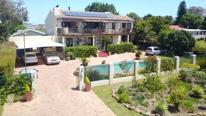 Una casa de dos pisos con balcón, paneles solares, entrada para vehículos y un jardín con diversas plantas.