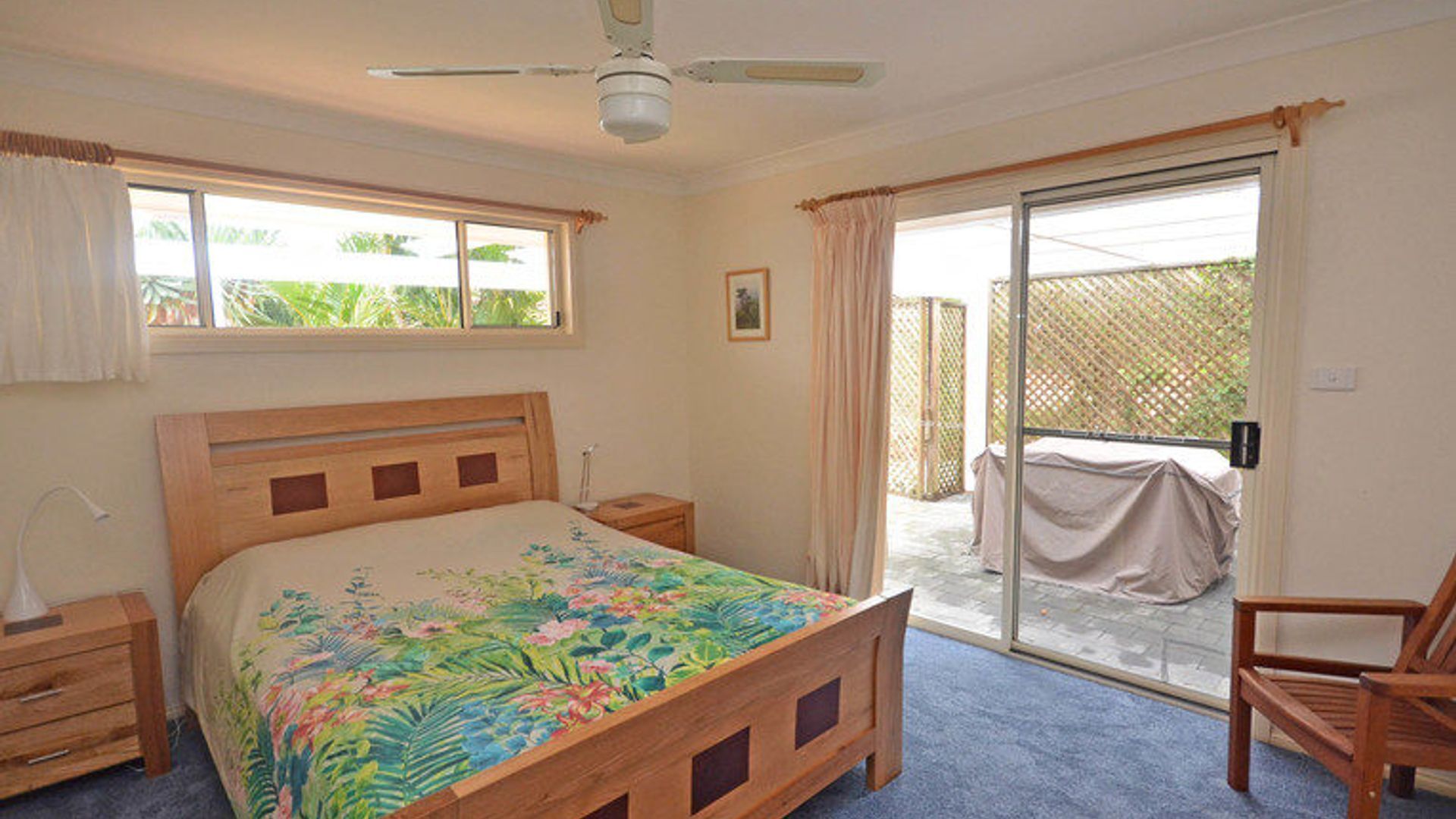 A bedroom with a wooden bed, a nightstand, a chair, a ceiling fan, and a sliding glass door leading to an outdoor area.