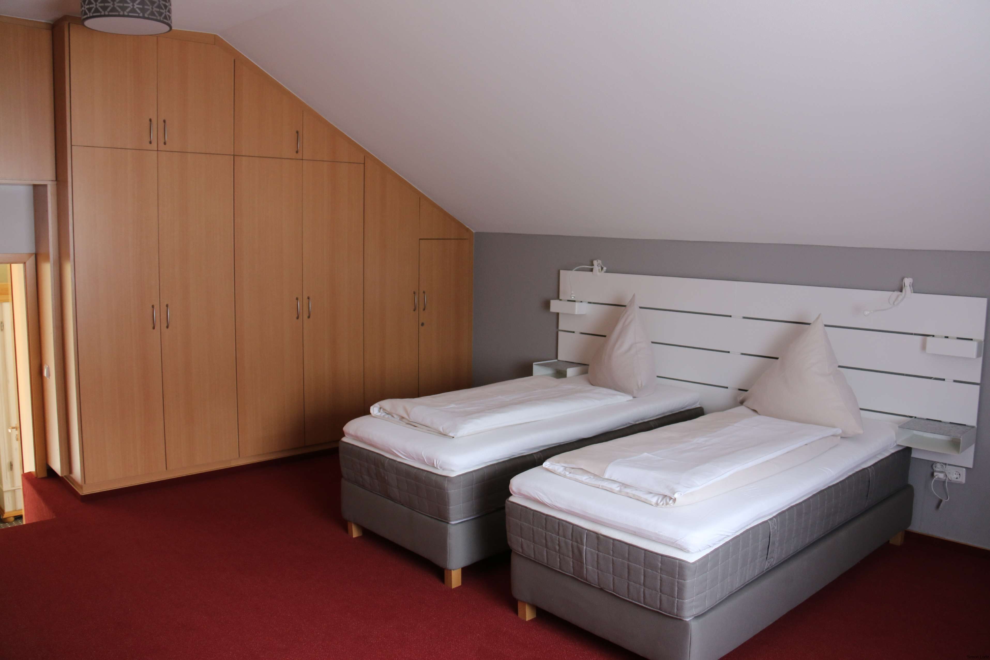 Ein Schlafzimmer mit zwei Einzelbetten, einem Holzschrank und einem roten Teppich.
