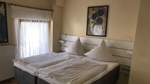 Una cama bien hecha con cabecera, una ventana con cortinas translúcidas y un cuadro en la pared.