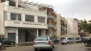 Un immeuble à plusieurs étages, avec une enseigne indiquant qu’il s’agit d’un hôpital, des voitures garées et un passage piétonnier.