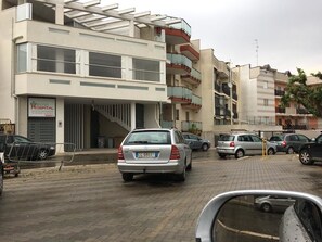 Een meerlaags gebouw met een ziekenhuisbord, geparkeerde auto's en een voetpad.