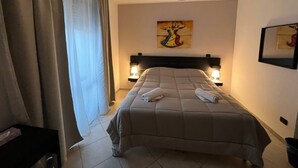 Hotellihuone, jossa on sänky, kaksi yöpöytälamppua, taulu seinällä ja ikkuna, jossa on verhot.
