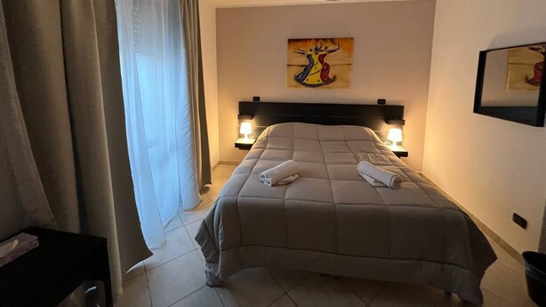 Une chambre d’hôtel avec un lit, deux lampes de chevet, un tableau au mur et une fenêtre avec des rideaux.