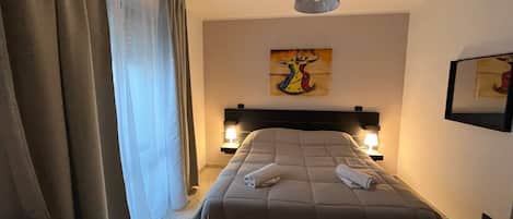 A hotel room with a bed, two bedside lamps, a painting on the wall, and a window with curtains.