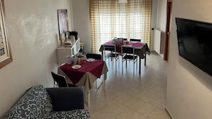 Un coin repas avec une table dressée pour deux personnes, un téléviseur fixé au mur et une fenêtre avec des rideaux.