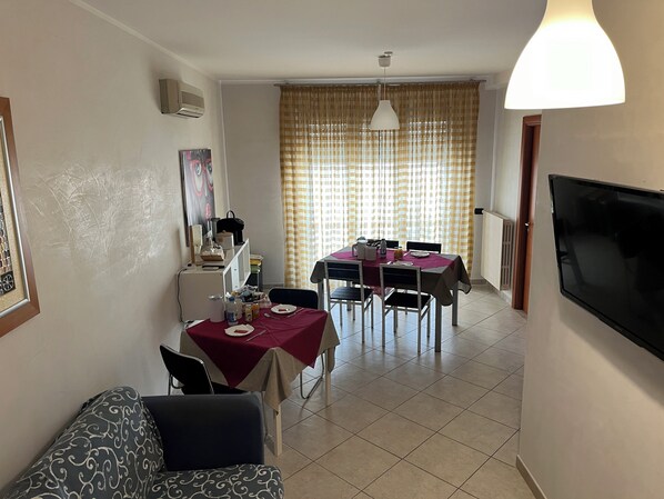 Un coin repas avec une table dressée pour deux personnes, un téléviseur fixé au mur et une fenêtre avec des rideaux.