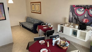 Un coin repas avec une table dressée pour deux personnes, un canapé et un tableau accroché au mur.