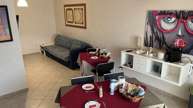 A dining area with a table set for two, a sofa, and a painting on the wall. - B&B Piazza Kolbe (Acquaviva delle Fonti)