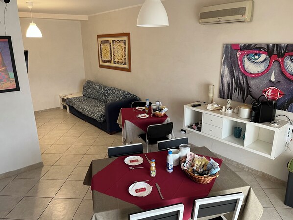 Un comedor con una mesa dispuesta para dos personas, un sofá y un cuadro en la pared.