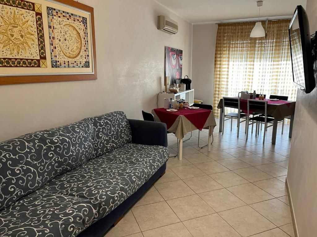 A living room with a sofa, a dining table with chairs, and a TV mounted on the wall.