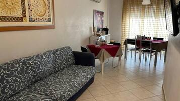 A living room with a sofa, a dining table with chairs, and a TV mounted on the wall.