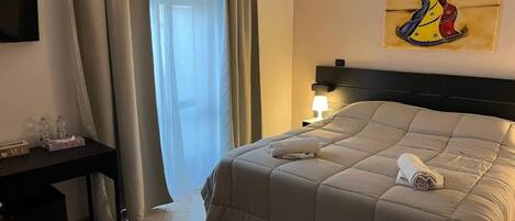 Een hotelkamer met een bed, een bureau, een lamp en een schilderij aan de muur.
