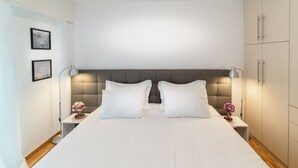 A neatly made bed with white linens, two bedside tables with lamps, and a wardrobe to the right.