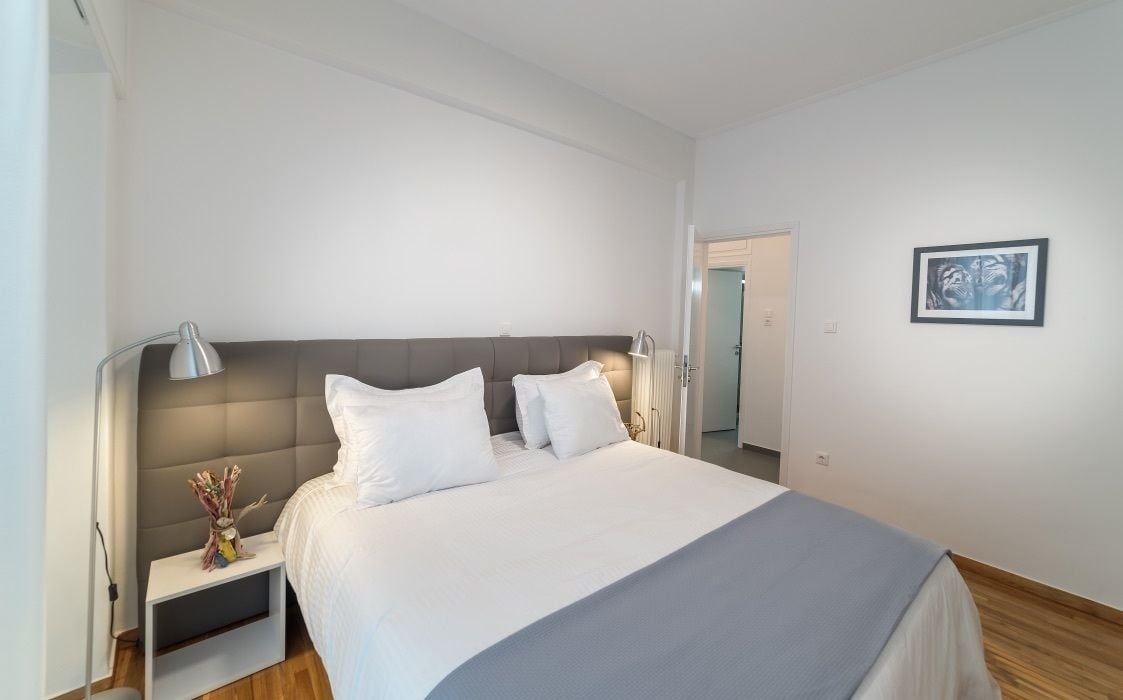 A modern hotel room with a large bed, a bedside table with a lamp, and a framed picture on the wall.
