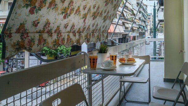 A balcony with a table set for two, a chair, and a potted plant.